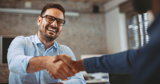 A man smiling and shaking the hand of someone who is out of frame.