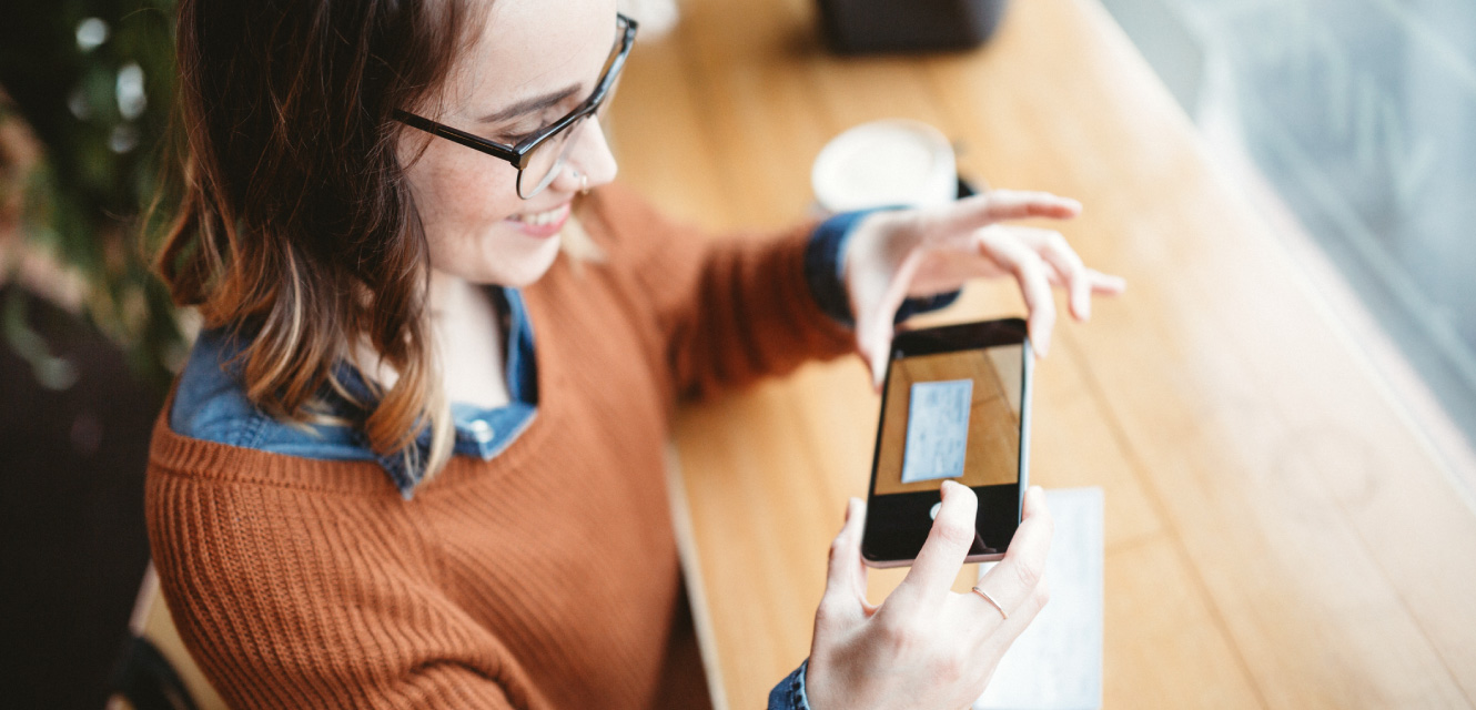 A young woman holding her phone over a check to deposit it. 